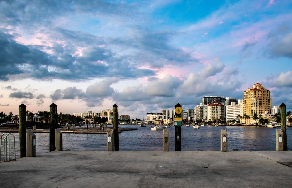 Scenic view of a vibrant waterfront city skyline at sunset with boats and clouds.